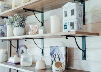 Kitchen wooden shelf with metal box with tea leaves in shape of house, ceramic jars, candles and accessories. Cozy interior in a country house.
