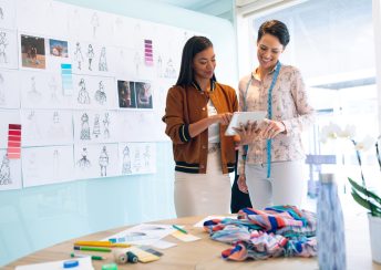 Front view of happy diverse female fashion designers discussing over digital tablet in a modern office